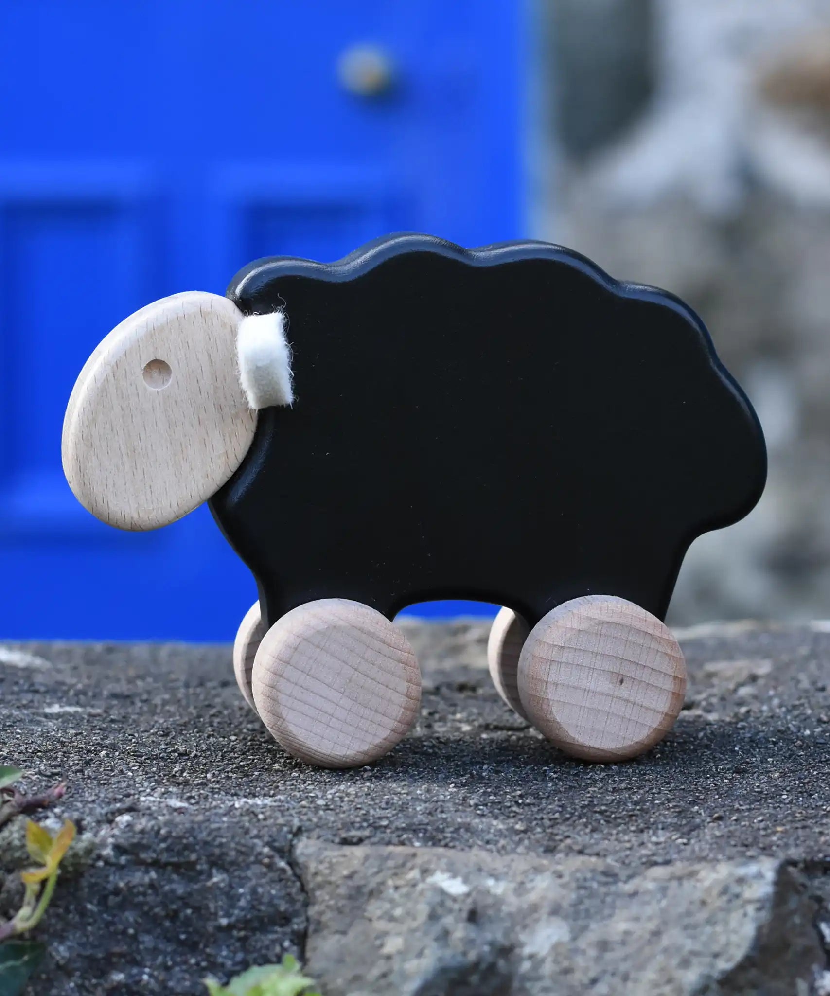 Bajo black sheep push along wooden toy on wheels placed on a stone wall outdoors.