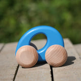 Bajo handmade wooden ellipse toy car in blue with unpainted wheels standing on a concrete surface
