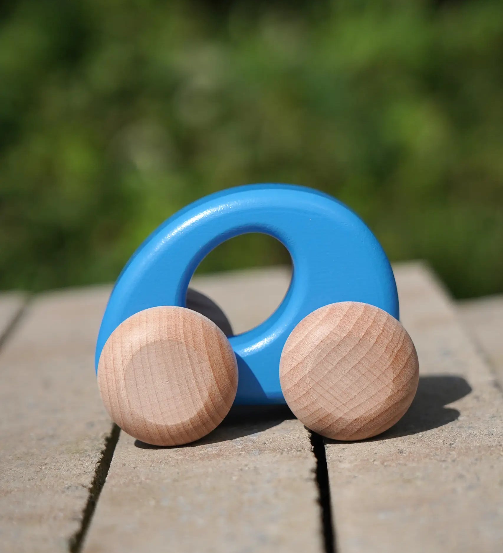 Bajo handmade wooden ellipse toy car in blue with unpainted wheels standing on a concrete surface