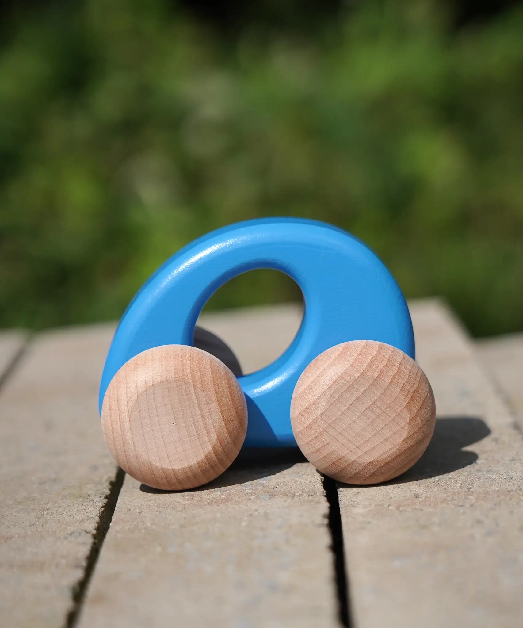 Bajo handmade wooden ellipse toy car in blue with unpainted wheels standing on a concrete surface