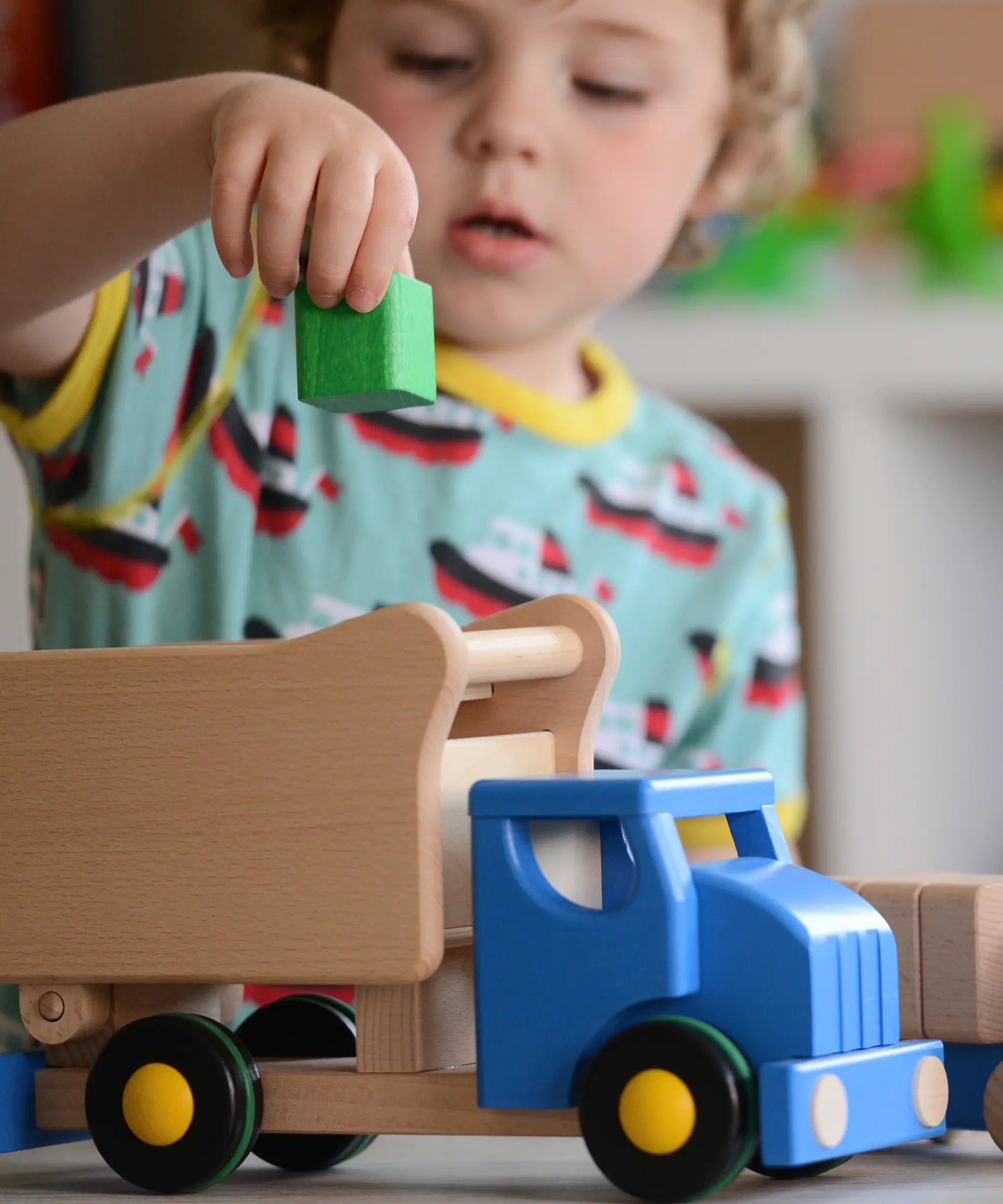Child playing with the Bajo blue tipper truck shape sorter placing a green cube into the slot at the top.