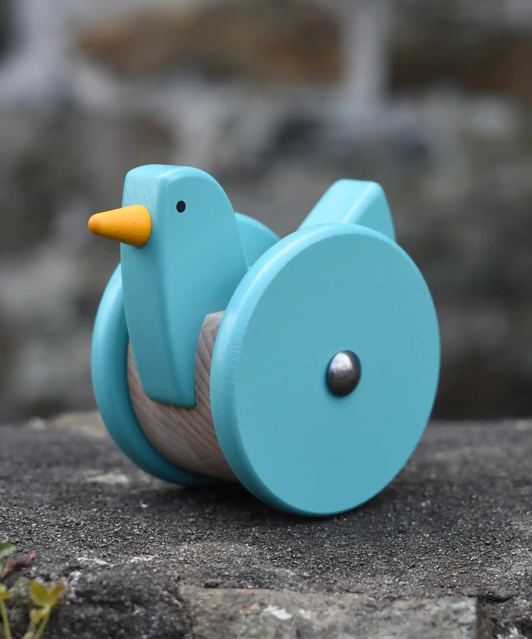 Bajo blue wobbling chicken push along toy placed on a stone wall.