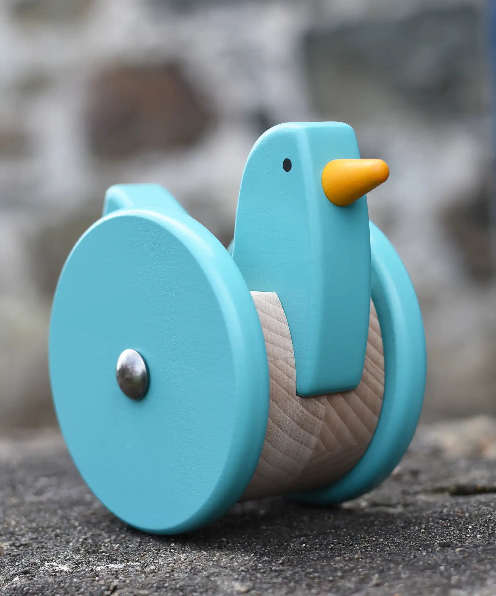 Front of the Bajo blue wobbling chicken push along toy placed on a stone wall.