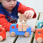A child placing the wooden blocks on the back on a blue Bajo truck