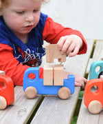 A child placing the wooden blocks on the back on a blue Bajo truck. This wooden truck is part of a wide range of Bajo wooden toy vehicles available at Babipur.