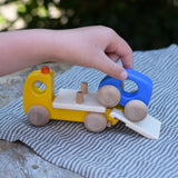 Bajo yellow breakdown lorry wooden toy with a child's hand driving the blue car up the ramp onto the trailer.