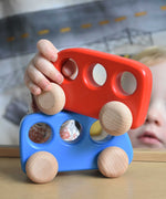A child's hand holding a red coloured bus, the child is placing it on a blue coloured bus. These heirloom quality toys by Bajo are part of a wide range of wooden toys available here at Babipur. 