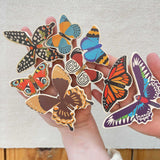 An adult holding all the butterfly shaped pieces from the Bajo World Of Butterflies Sorter Puzzle in their hand. This puzzle has butterfly shaped pieces that are decorated on both sides that slot into the coordinating shapes on the base. These heirloom quality toys by Bajo are part of a wide range of wooden toys available here at Babipur.