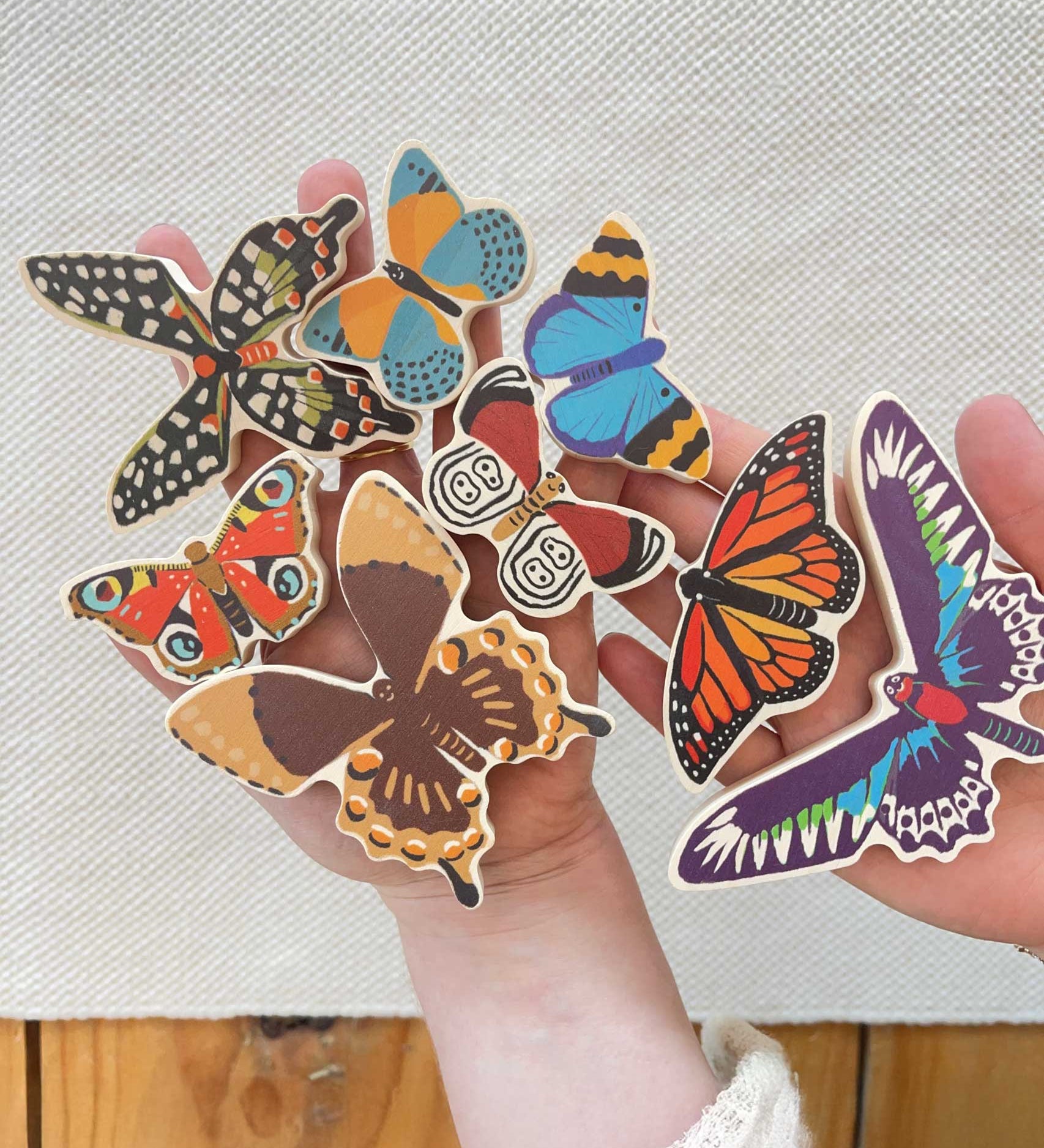An adult holding all the butterfly shaped pieces from the Bajo World Of Butterflies Sorter Puzzle in their hand. This puzzle has butterfly shaped pieces that are decorated on both sides that slot into the coordinating shapes on the base. These heirloom quality toys by Bajo are part of a wide range of wooden toys available here at Babipur.