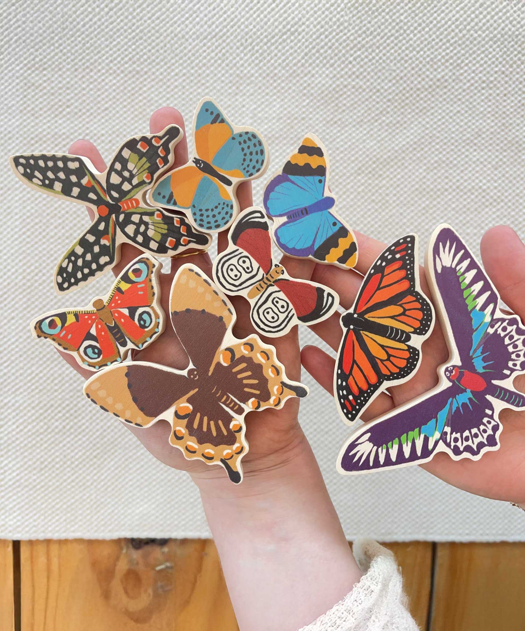An adult holding all the butterfly shaped pieces from the Bajo World Of Butterflies Sorter Puzzle in their hand. This puzzle has butterfly shaped pieces that are decorated on both sides that slot into the coordinating shapes on the base. These heirloom quality toys by Bajo are part of a wide range of wooden toys available here at Babipur.