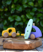 Bajo yellow car and purple camper wooden toy vehicle with green surfboard. the green surfboard is being rested against the camper/