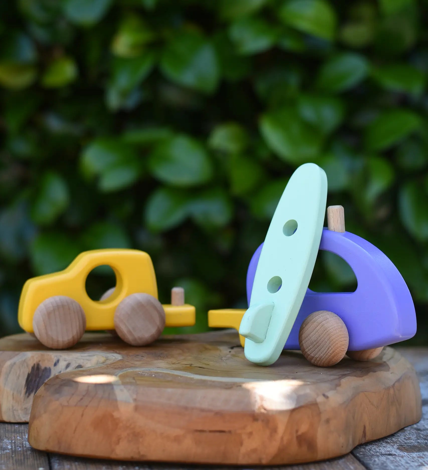 Bajo yellow car and purple camper wooden toy vehicle with green surfboard. the green surfboard is being rested against the camper/