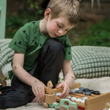 A child kneeling down playing with the Bajo mint green 4x4 car and horse trailer wooden toy. He is attaching the trailer to they car.