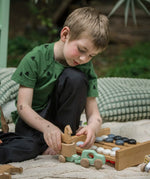 A child kneeling down playing with the Bajo mint green 4x4 car and horse trailer wooden toy. He is attaching the trailer to they car.