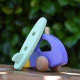 Green surfboard from the Bajo yellow car and purple camper wooden toy vehicle set resting on the camper.