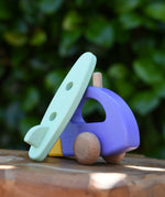 Green surfboard from the Bajo yellow car and purple camper wooden toy vehicle set resting on the camper.