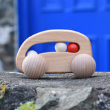 Bajo natural wooden toy car with beads push along toy placed on a stone wall outdoors. 