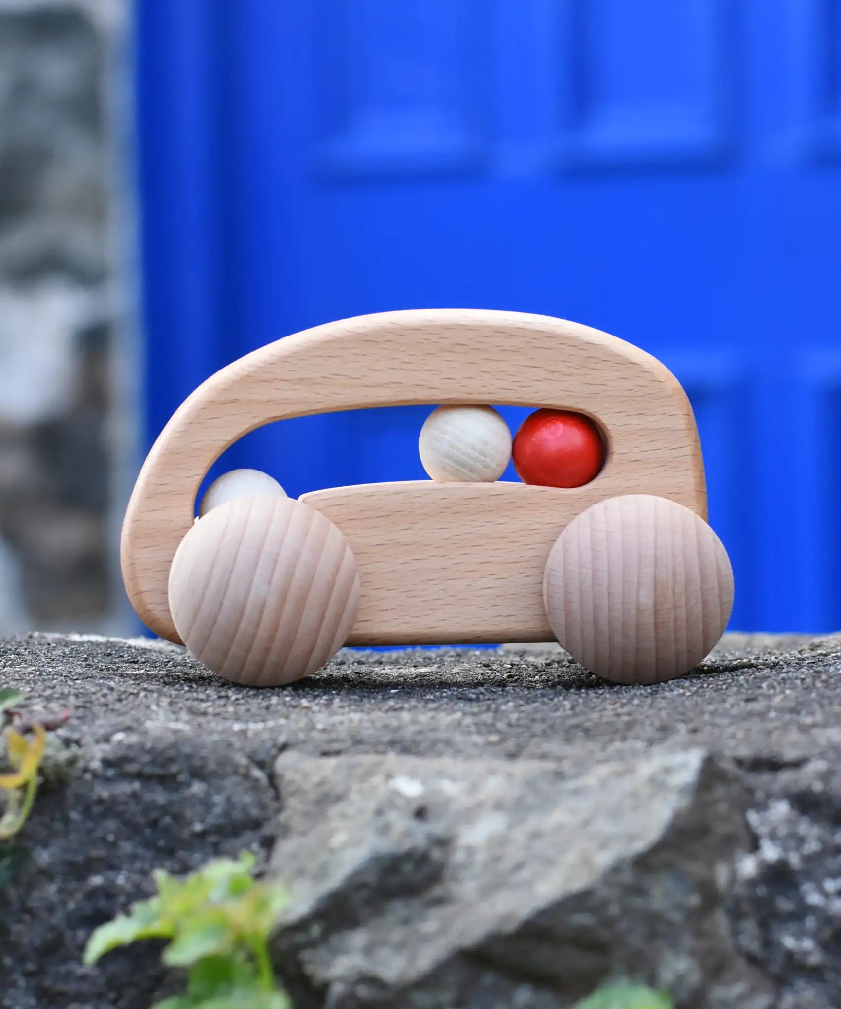 Bajo natural wooden toy car with beads push along toy placed on a stone wall outdoors. 