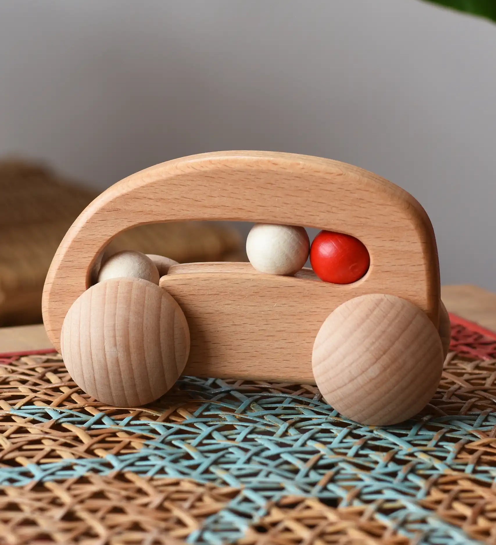 Bajo natural wooden car with beads push along toy on a rattan stool in the  Babipur playroom. 