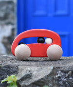 Bajo red wooden toy car with beads push along toy placed on a stone wall outdoors. 