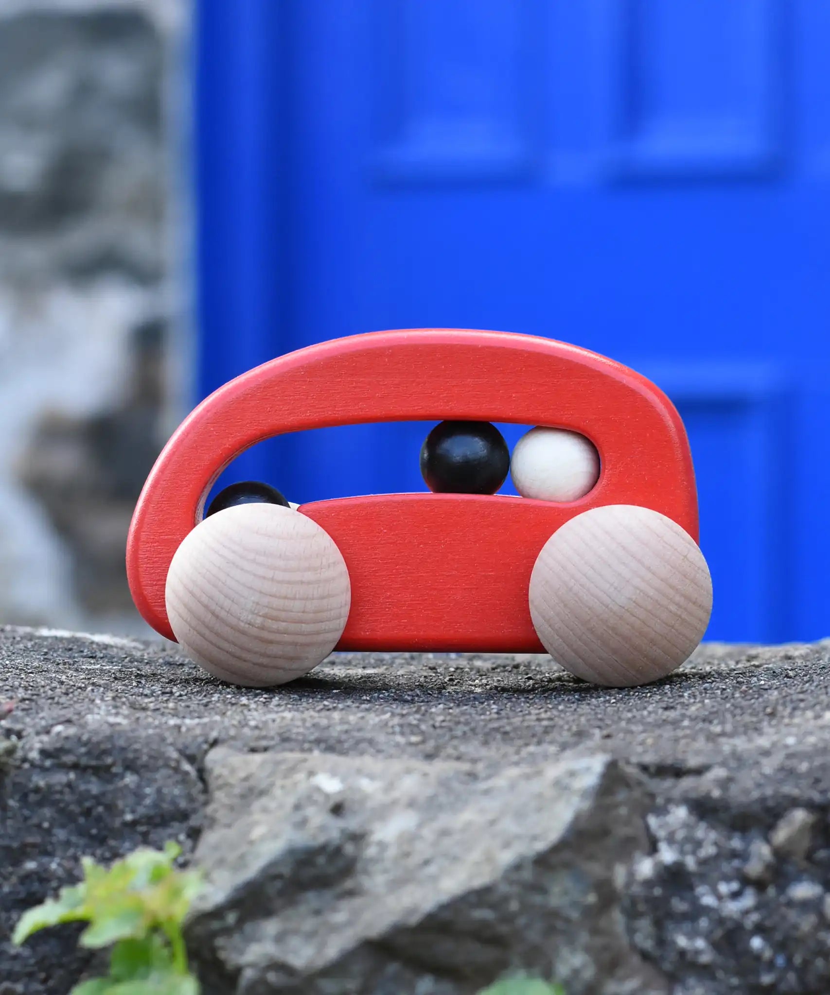 Bajo red wooden toy car with beads push along toy placed on a stone wall outdoors. 