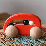 Bajo red wooden car with beads push along toy on a rattan stool in the  Babipur playroom. 