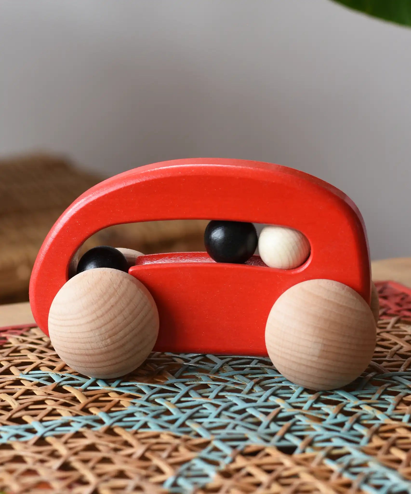 Bajo red wooden car with beads push along toy on a rattan stool in the  Babipur playroom. 
