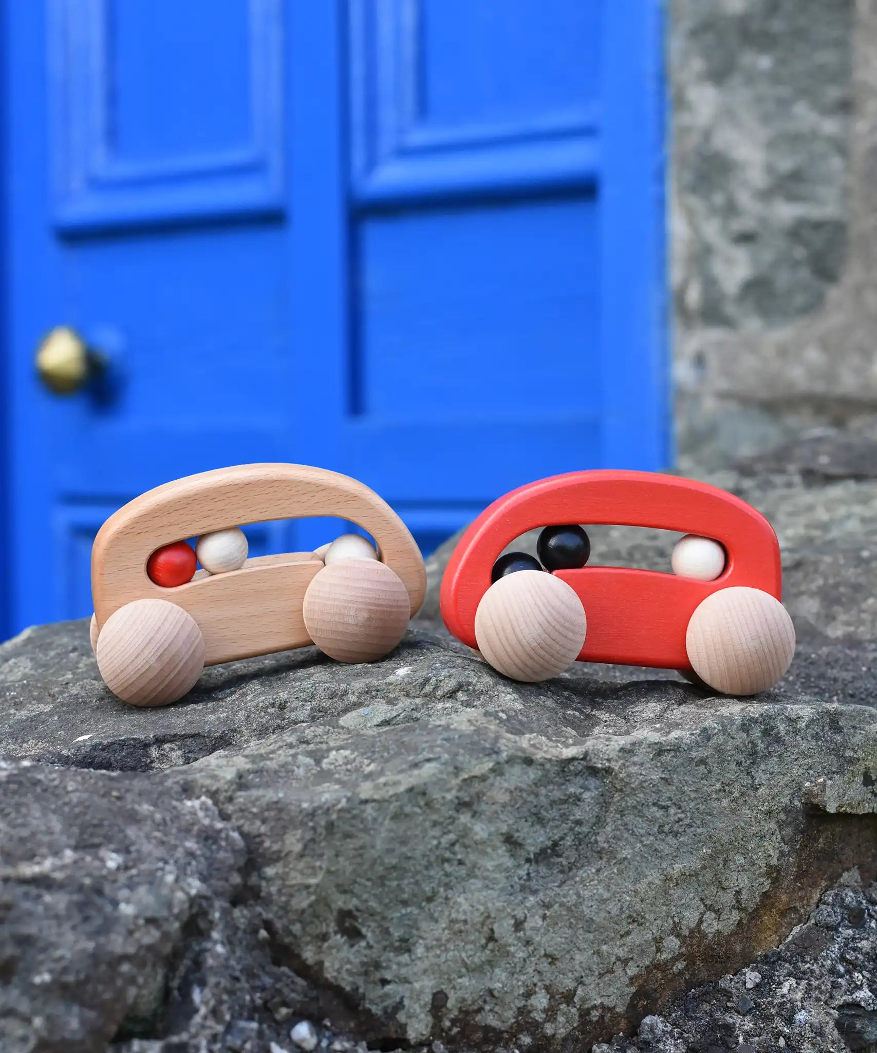 Bajo wooden toy cars with beads push along toys placed on a stone wall outdoors. 