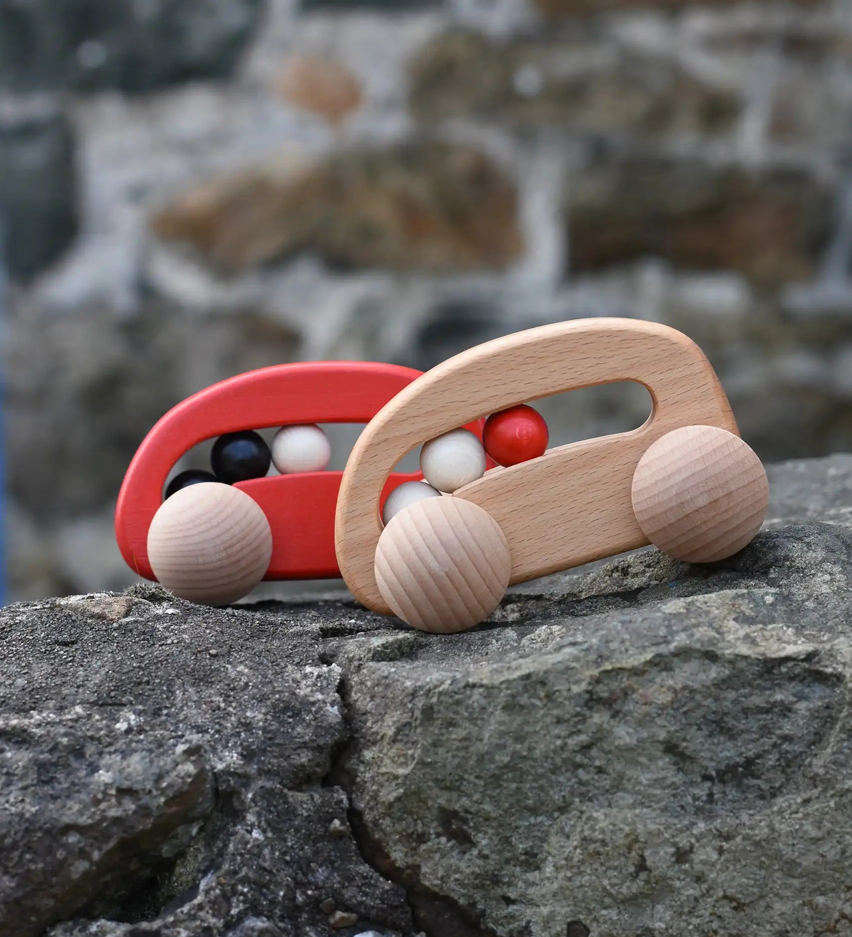 Bajo wooden toy cars with beads push along toys placed on a stone wall outdoors. 