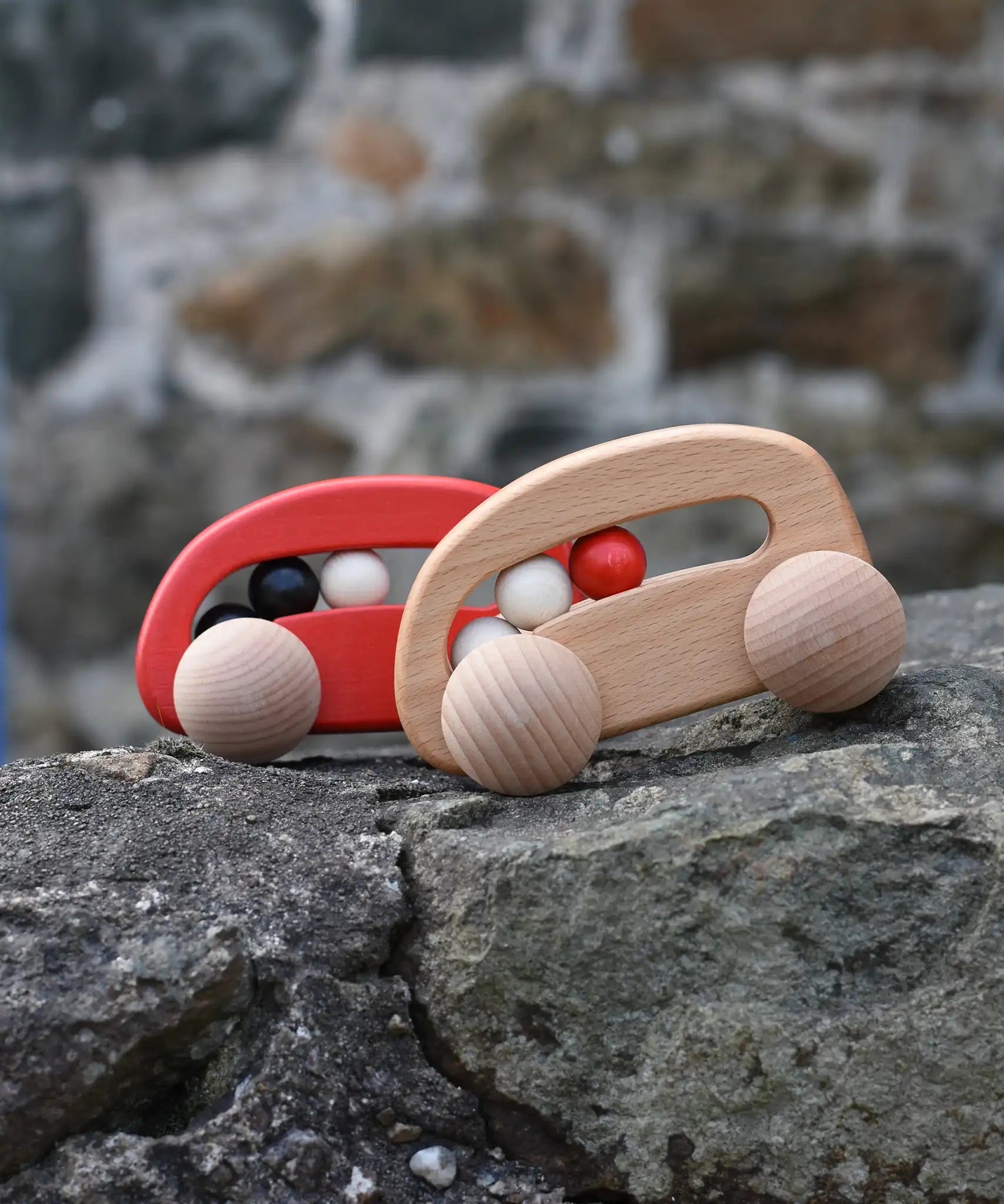 Bajo wooden toy cars with beads push along toys placed on a stone wall outdoors. 