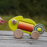 Colorful wooden baby chameleon toy being pulled on a wooden surface with a blurred natural background