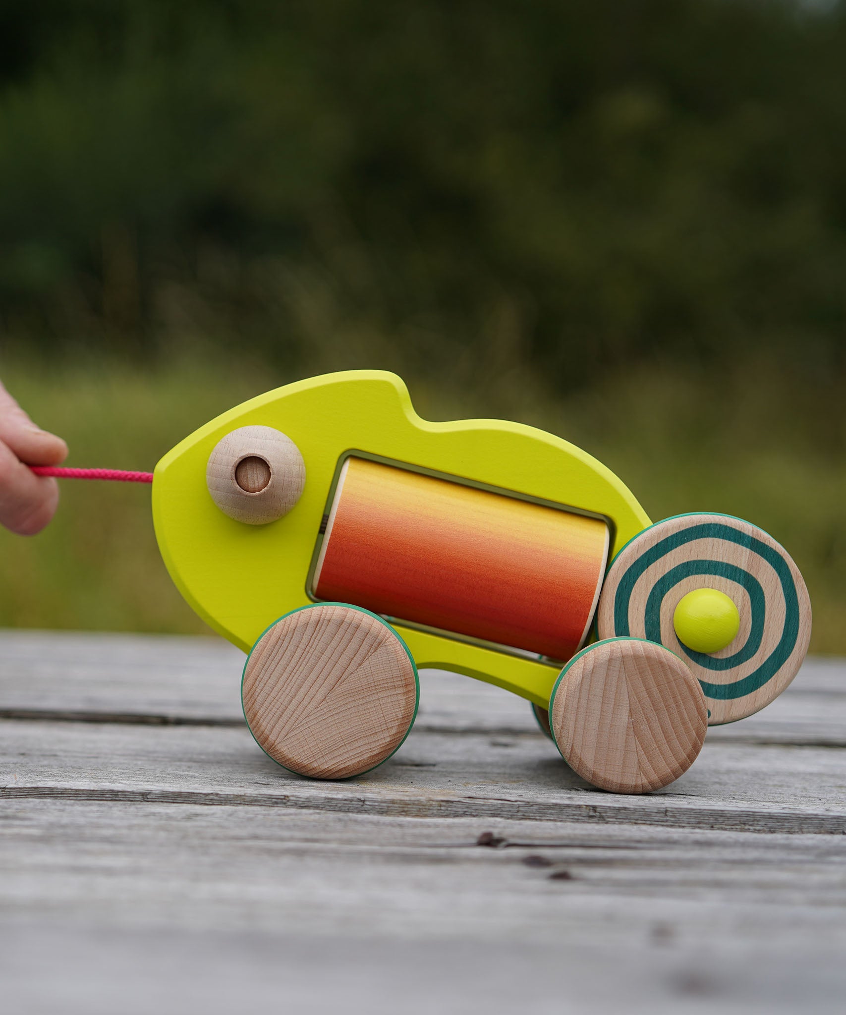Colorful wooden baby chameleon toy being pulled on a wooden surface with a blurred natural background