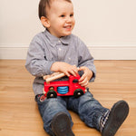 Child sat on a wooden floor holding a Bajo wooden fire engine toy
