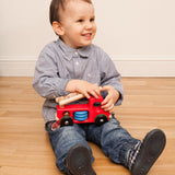 Child sat on a wooden floor holding a Bajo wooden fire engine toy