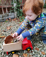 Young boy putting leaves and stones into the back of the Bajo wooden shape sorter tipper truck
