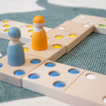 Close up of two wooden peg doll figures on top of the Bajo kids wooden XXL dominos game on a blue and white carpet