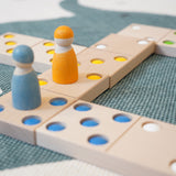 Close up of two wooden peg doll figures on top of the Bajo kids wooden XXL dominos game on a blue and white carpet