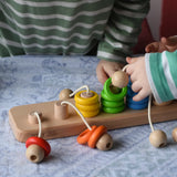 Bajo rope abacus toy with 10 pegs and coloured and natural wooden rings attached with ropes. Children lifting the rings off the pegs.