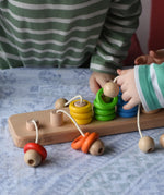 Bajo rope abacus toy with 10 pegs and coloured and natural wooden rings attached with ropes. Children lifting the rings off the pegs.