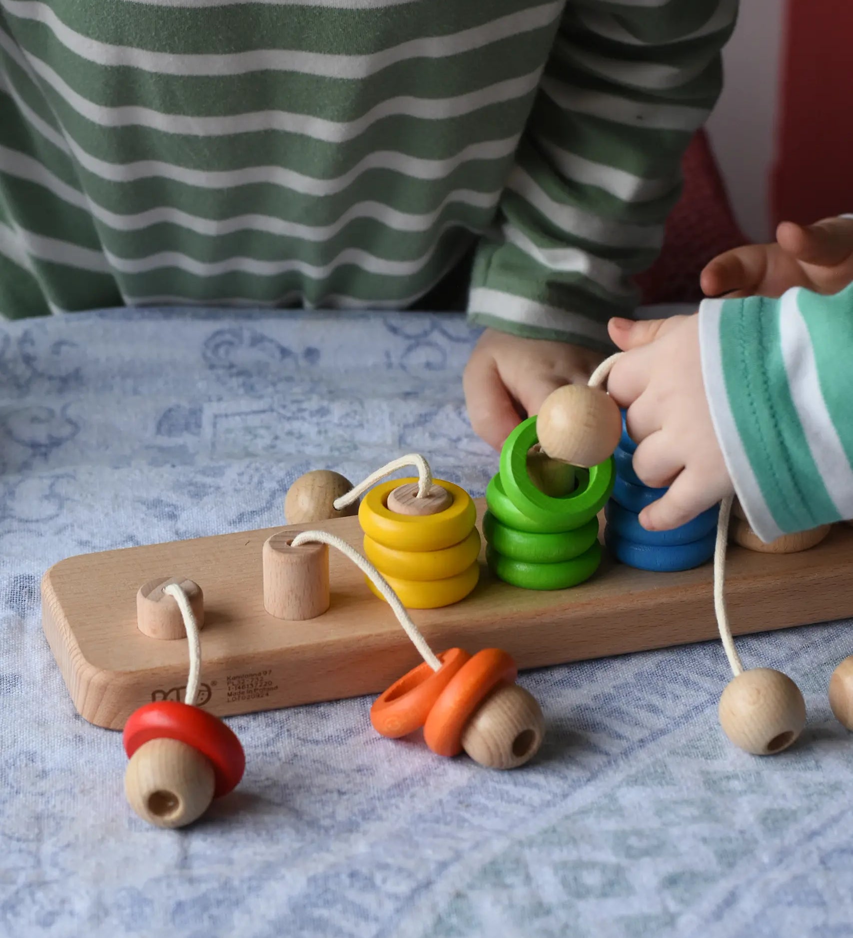 Bajo rope abacus toy with 10 pegs and coloured and natural wooden rings attached with ropes. Children lifting the rings off the pegs.