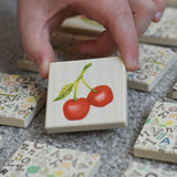 A child holding a tile from the Bajo Wooden Tiles Memory Game. The tile has an illustration of a cherry on it. These heirloom quality toys by Bajo are part of a wide range of wooden toys available here at Babipur. 