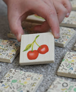 A child holding a tile from the Bajo Wooden Tiles Memory Game. The tile has an illustration of a cherry on it. These heirloom quality toys by Bajo are part of a wide range of wooden toys available here at Babipur. 
