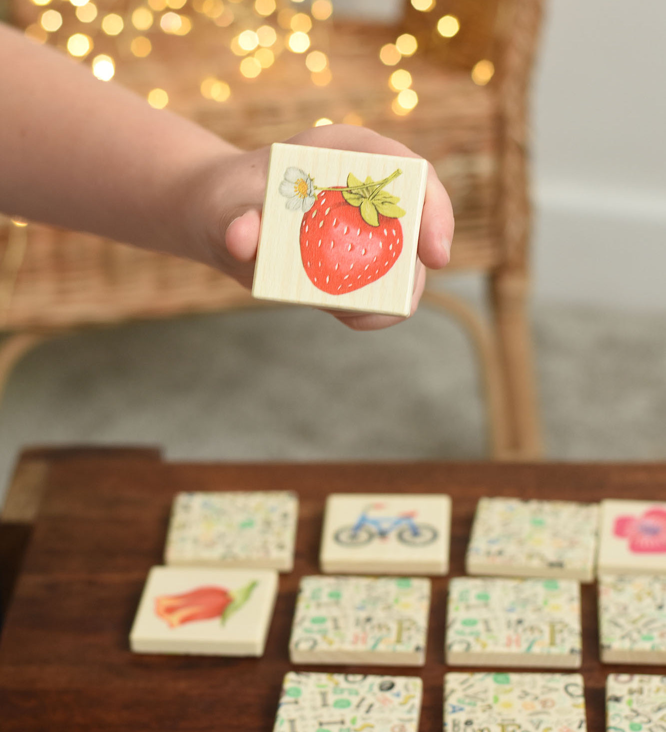 A child holding up a tile from the Bajo Wooden Tiles Memory Game. The tile has an illustration of a strawberry on it. These heirloom quality toys by Bajo are part of a wide range of wooden toys available here at Babipur. 