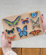 The Bajo World Of Butterflies Sorter Puzzle shown in an adult's hand. This puzzle has butterfly shaped pieces that are decorated on both sides that slot into the coordinating shapes on the base. These heirloom quality toys by Bajo are part of a wide range of wooden toys available here at Babipur.