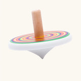 Side profile of Bajo colourful circles spinning top wooden toy. White painted wooden base with a rainbow stripe decorated top and a natural wood handle.