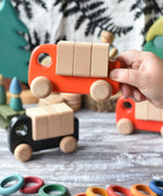 An adult's hand holding up the coral coloured Bajo truck with blocks