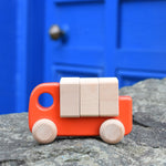 A coral coloured Bajo truck with blocks placed on a stone wall 