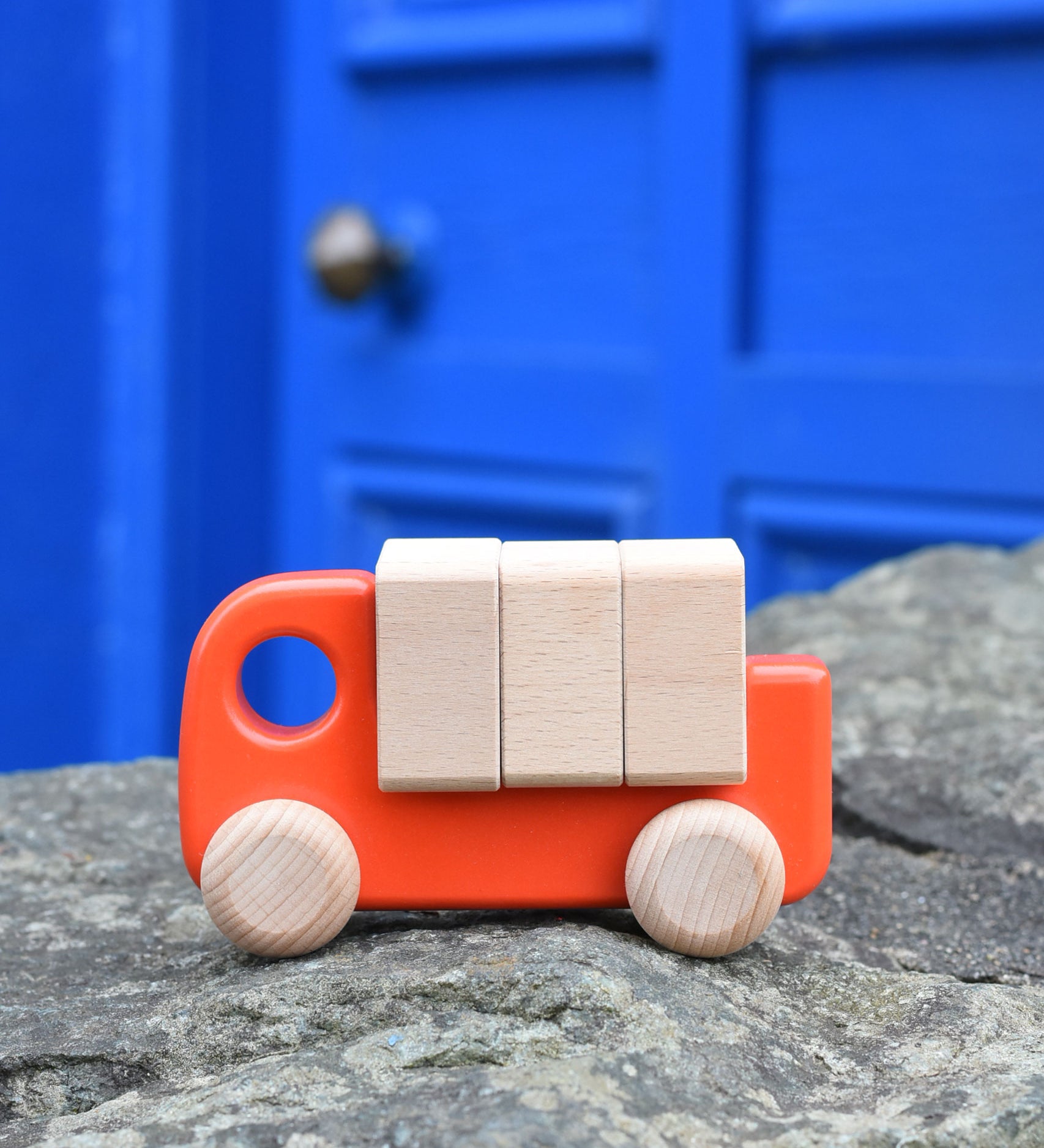 A coral coloured Bajo truck with blocks placed on a stone wall 