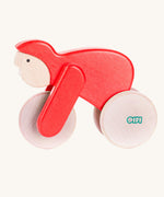 A red Bajo Velo cyclist wooden toy. This wooden toy is part of a wide range of push along toys available at Babipur.