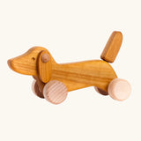 Bajo Natural Dachshund Puppy in unpainted natural wood, a push-along toy for toddlers with floppy ears, an upright tail, and four wooden wheels, available online from Babipur.